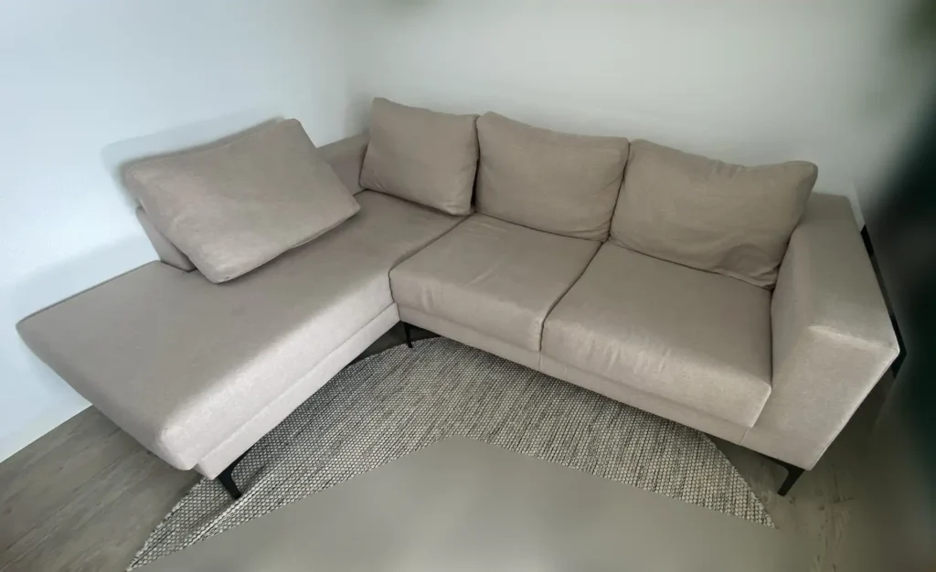Moderno sofá chaiselongue beige claro con manchas localizadas antes de su limpieza en Retiro