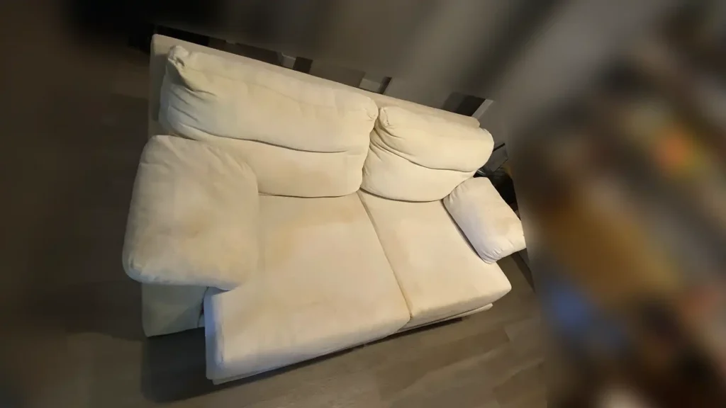 Sofá de dos plazas color crema con tela de relieve y manchas de suciedad en Arganzuela
