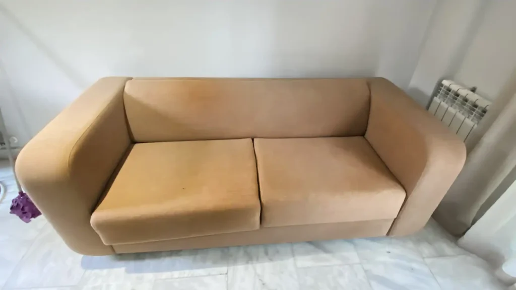 Estado inicial del sofá de microfibra beige en Quintana: oscurecimiento uniforme en el respaldo, apoyabrazos y cercos de grasa por alto tránsito de huéspedes.